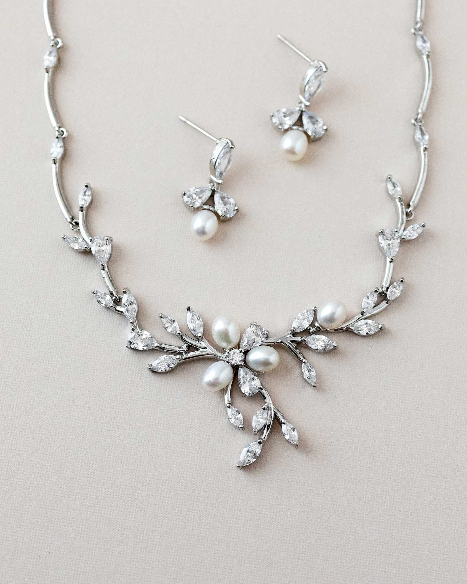 A bridal jewelry necklace set with an ivory pearl flower and teardrop and marquise CZ jewels, including a matching bracelet and earrings.