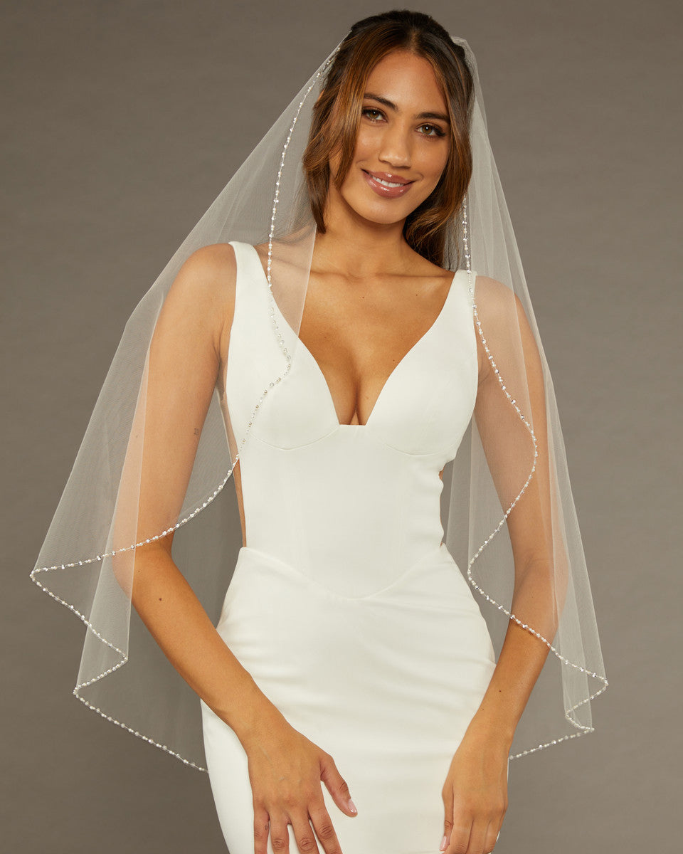 Fingertip Veil with Pearls and Sequins Woman wearing a wedding dress with a sheer veil against a neutral background