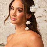 Light Ivory Organza Flower Earrings A woman with brown hair wearing a fabric flower hair accessory and matching tassel earrings, shown against a textured light beige wall.
