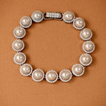 Tennis Style Pearl CZ Bracelet A pearl and crystal bracelet arranged in a circle on a textured brown background. The bracelet features large off-white pearls surrounded by small clear crystals, with a silver-toned clasp at the top.