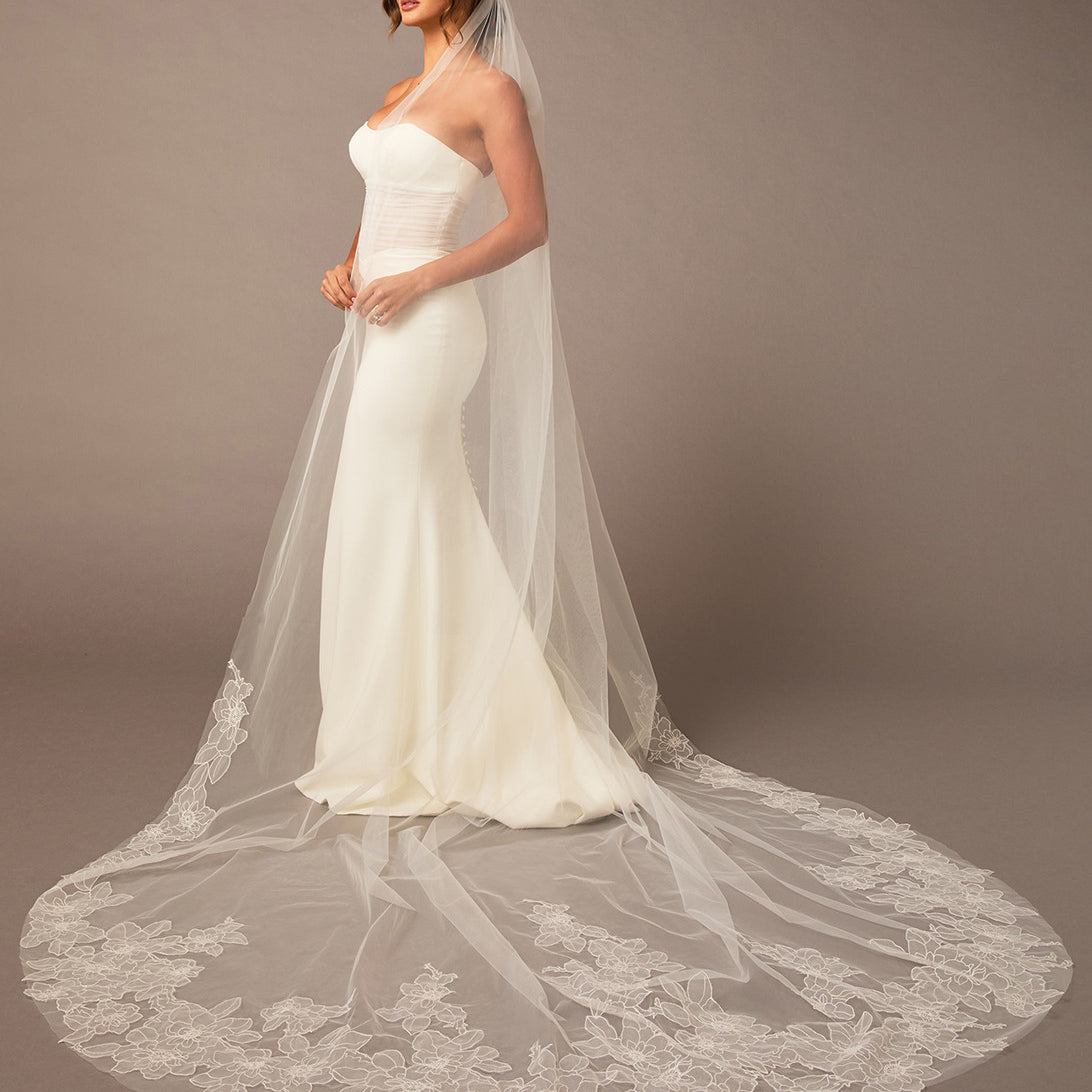 Woman wearing a white wedding dress with a long veil against a brown background Royal Cathedral Bridal Veil Floral Embroidered Lace - Cassandra Lynne