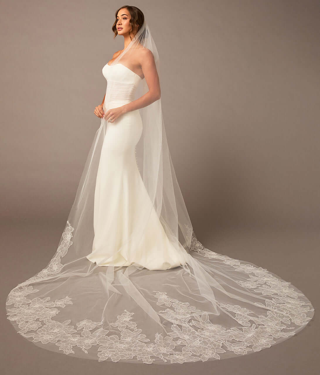 Woman wearing a white wedding dress with a long veil against a brown background Royal Cathedral Bridal Veil Floral Embroidered Lace - Cassandra Lynne