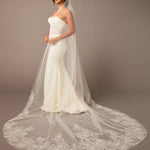 Woman wearing a white wedding dress with a long veil against a brown background Royal Cathedral Bridal Veil Floral Embroidered Lace - Cassandra Lynne