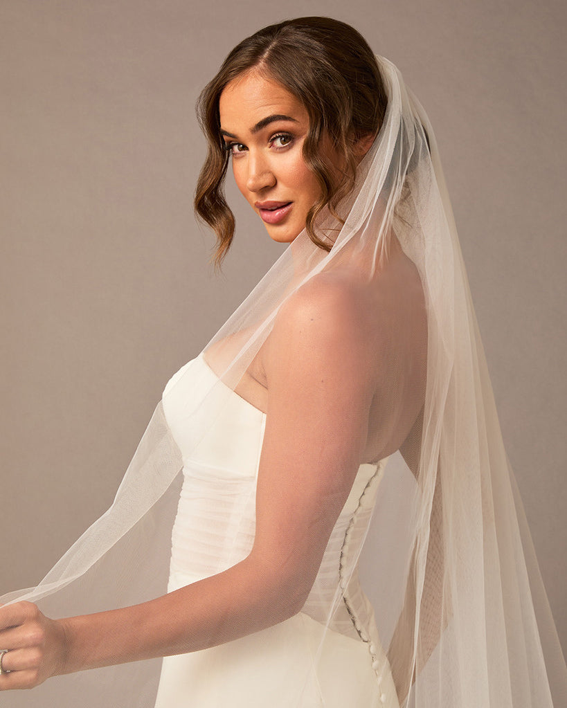Woman wearing a white wedding dress with a long veil against a brown background Royal Cathedral Bridal Veil Floral Embroidered Lace - Cassandra Lynne