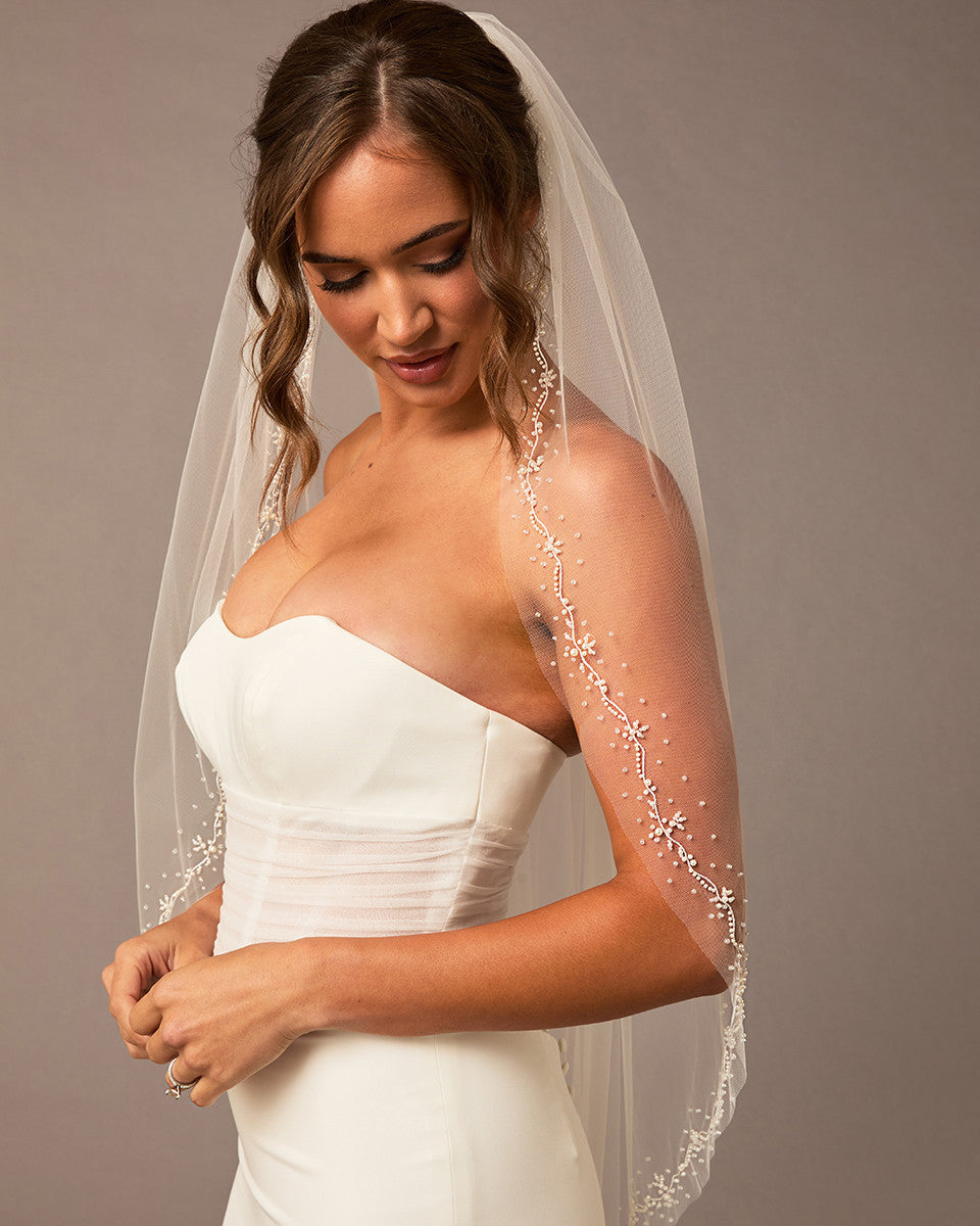 Pearl Wave Fingertip Bridal Veil Woman wearing a wedding dress with a veil against a neutral background