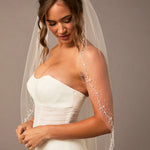 Pearl Wave Fingertip Bridal Veil Woman wearing a wedding dress with a veil against a neutral background