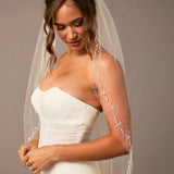 Pearl Wave Fingertip Bridal Veil Woman wearing a wedding dress with a veil against a neutral background