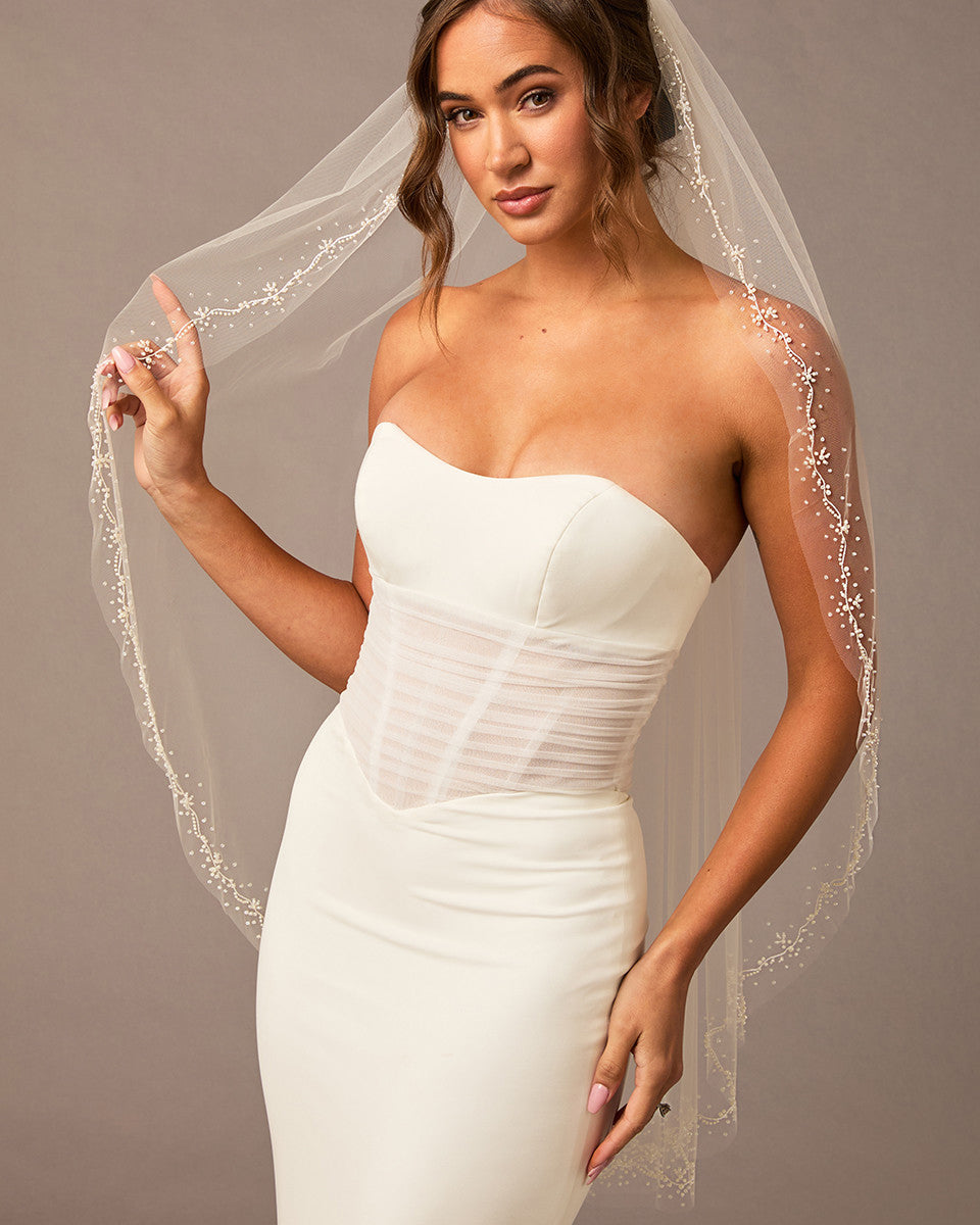 Pearl Wave Fingertip Bridal Veil Woman wearing a  strapless dress and veil against a neutral background
