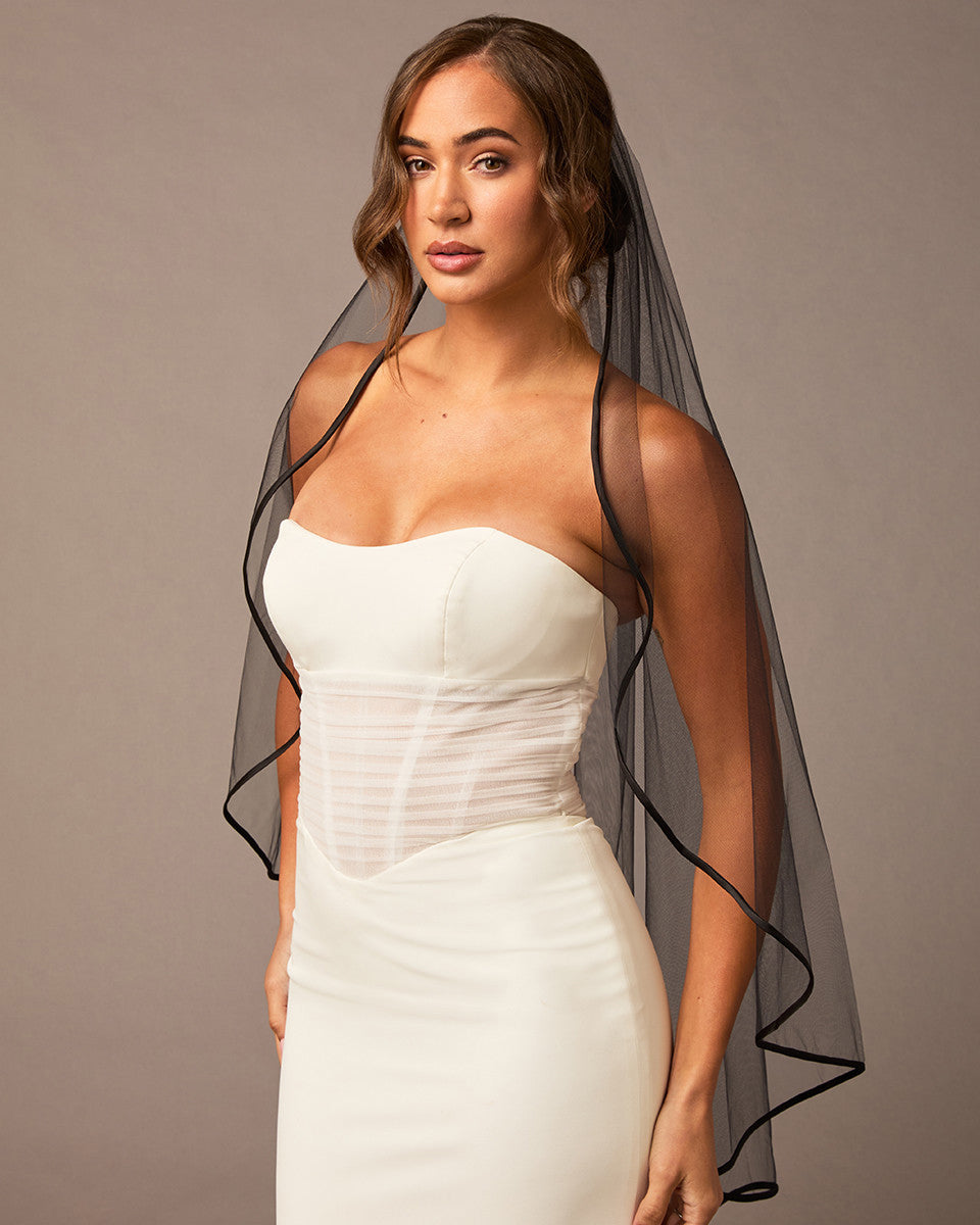 Woman wearing a ivory strapless dress with a black veil against a plain background