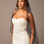 Woman wearing a ivory strapless dress with a black veil against a plain background