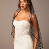 Woman wearing a ivory strapless dress with a black veil against a plain background