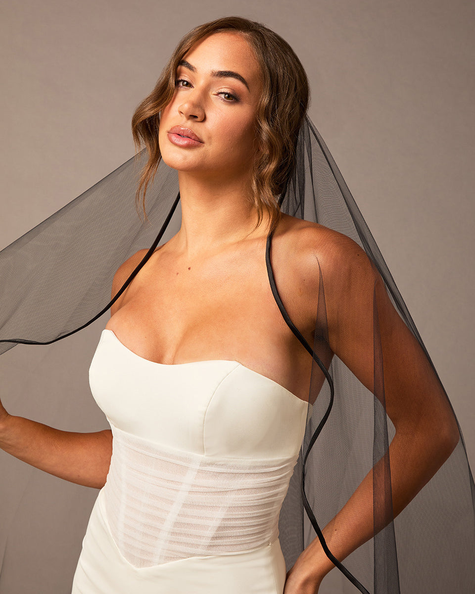 Woman wearing a dress with a black veil against a neutral background