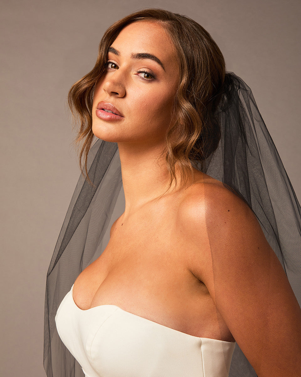 Woman wearing a  strapless dress with a gray veil against a neutral background