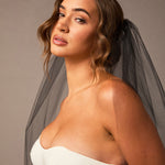 Woman wearing a  strapless dress with a gray veil against a neutral background