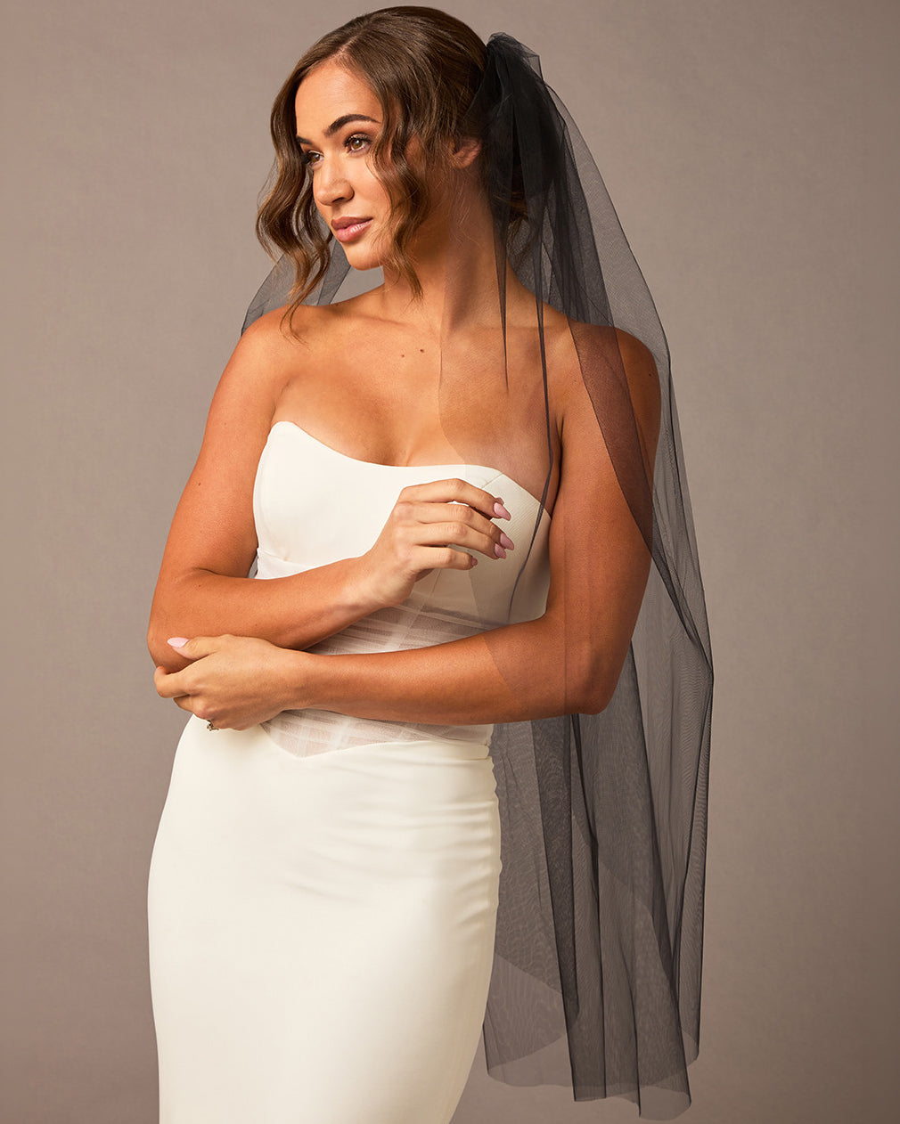 Woman wearing a strapless dress with a black veil against a plain background
