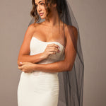 Woman wearing a strapless dress with a black veil against a plain background