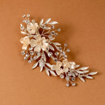 Porcelain Ivory Flowers and Crystals Bridal Clip A floral bridal hair claw clip featuring cream-colored faux flowers and silver-toned leaves, accented with clear rhinestones, displayed on a warm brown background.