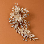 Porcelain Ivory Flowers and Crystals Bridal Clip A floral and leaf hair accessory brooch featuring cream-colored faux flowers, silver-toned leaves, and clear rhinestones, displayed on a warm brown background.
