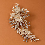 Porcelain Ivory Flowers and Crystals Bridal Clip A floral and leaf hair accessory brooch featuring cream-colored faux flowers, silver-toned leaves, and clear rhinestones, displayed on a warm brown background.