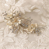 Porcelain Ivory Flowers and Crystals Bridal Clip A delicate bridal hairpiece featuring cream satin flowers, small crystal beads, and silver-toned leaves, displayed on a matching cream lace fabric background.