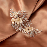 Porcelain Ivory Flowers and Crystals Bridal Clip A floral bridal hair accessory featuring cream and champagne embroidered flowers, silver-toned leaves, and clear rhinestones, displayed on draped champagne satin fabric.