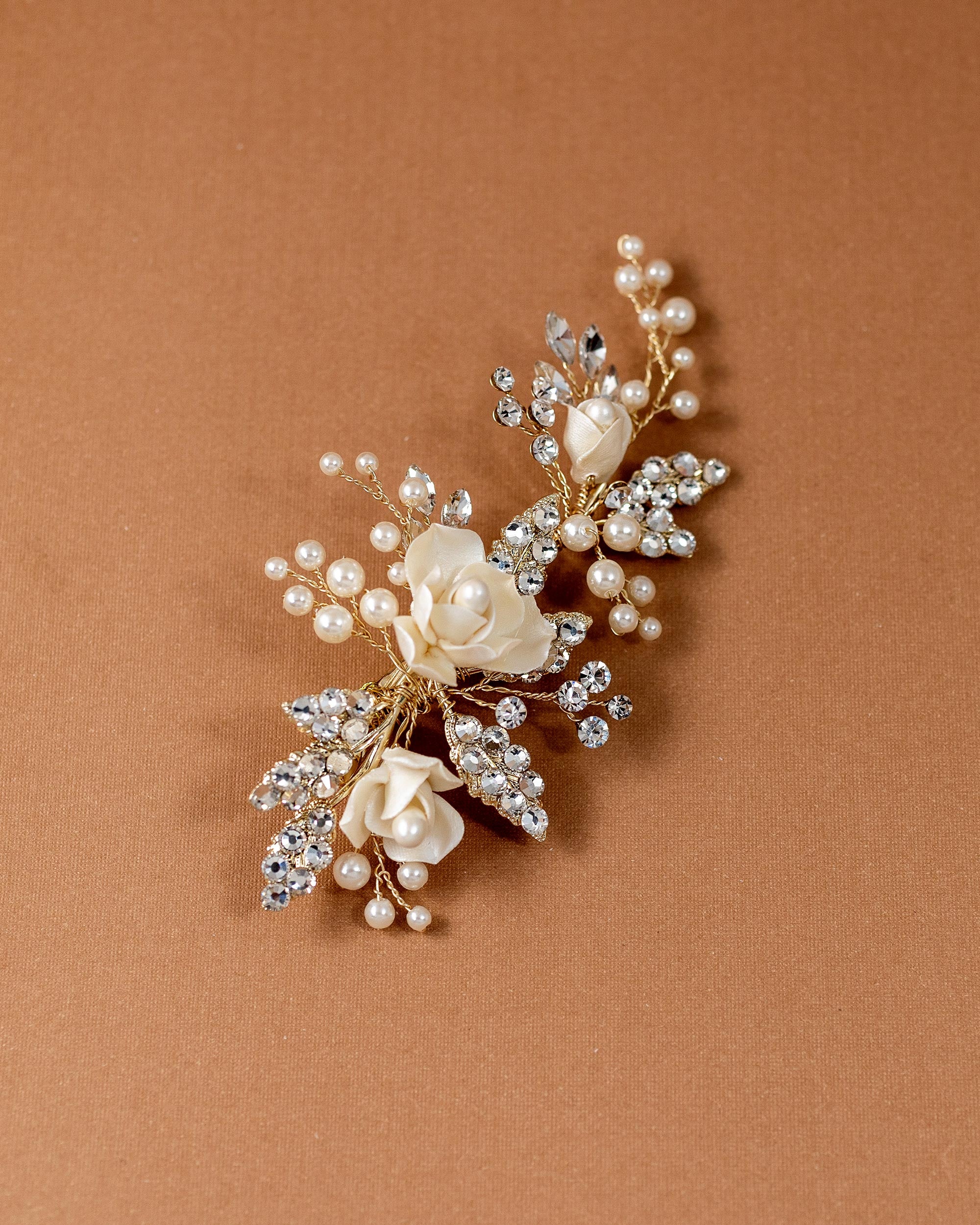Pearled Porcelain Flower Hair Clip A gold-toned floral hair accessory featuring cream-colored faux pearls and clear rhinestones, arranged in a cascading floral design on a solid brown background.