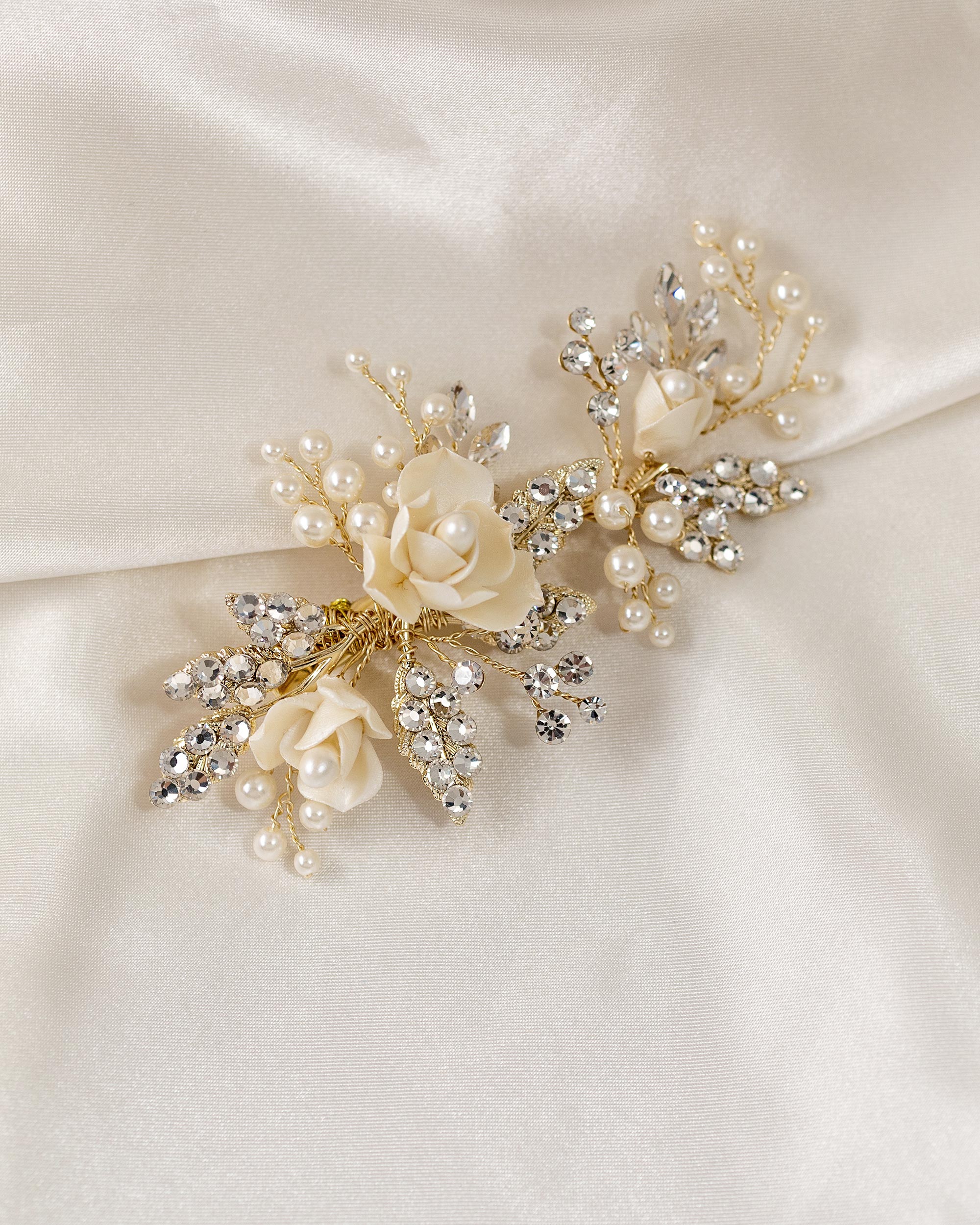 Pearled Porcelain Flower Hair Clip A gold bridal hairpin brooch featuring cream-colored faux roses, white pearls, and clear rhinestones, displayed on a draped cream satin fabric.