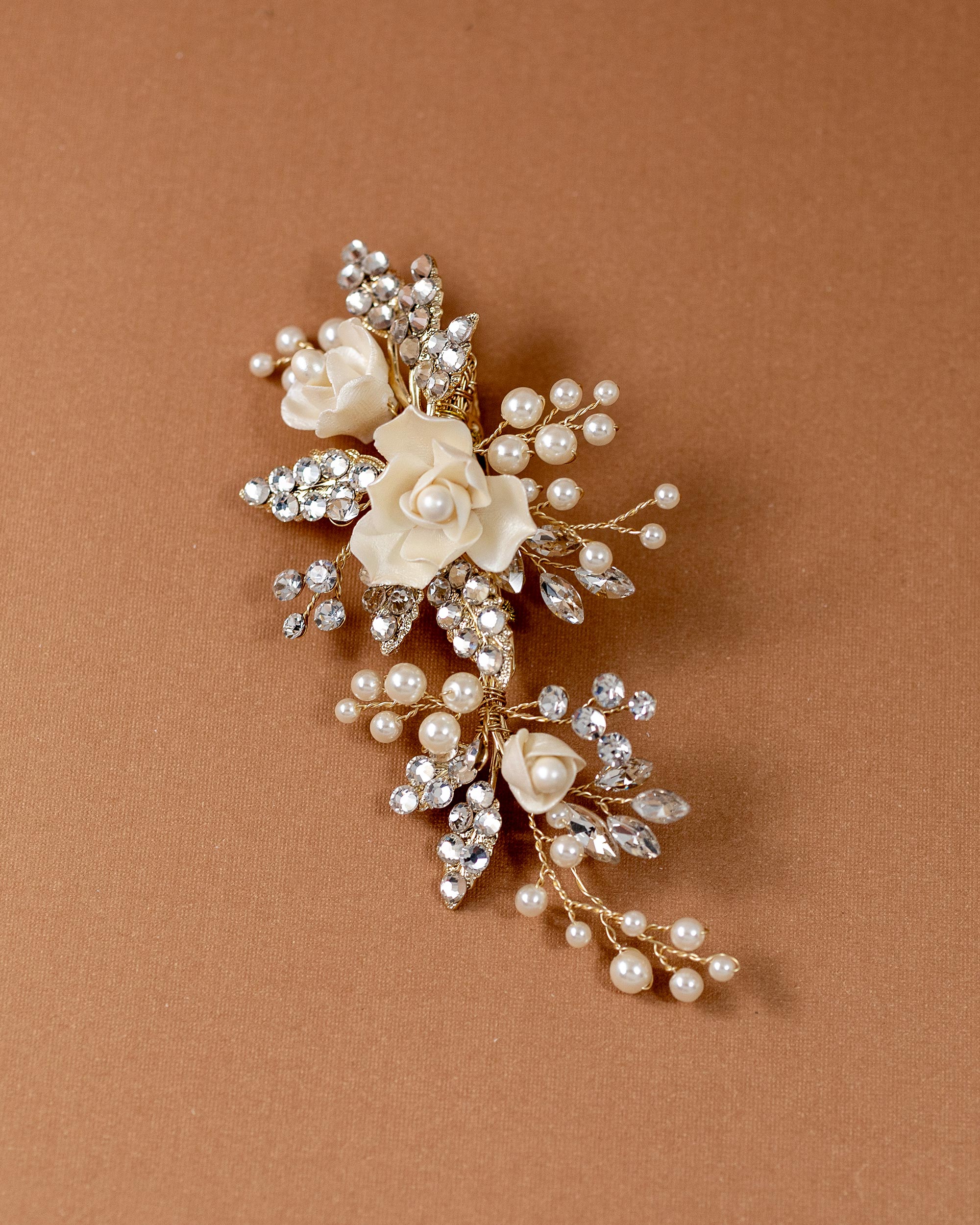 Pearled Porcelain Flower Hair Clip A gold-toned floral hair pin featuring cream-colored faux pearls and clear rhinestones, displayed on a solid warm brown background.