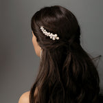 Woman with long dark hair styled with a pearl hairpiece against a gray background
