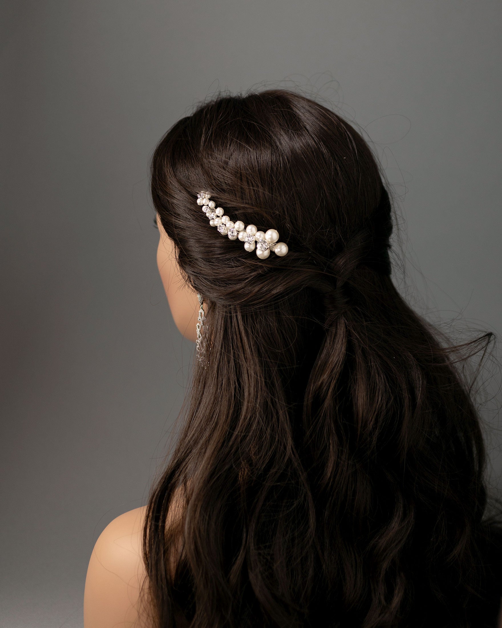 Woman with long dark hair styled with a pearl hairpiece against a gray background