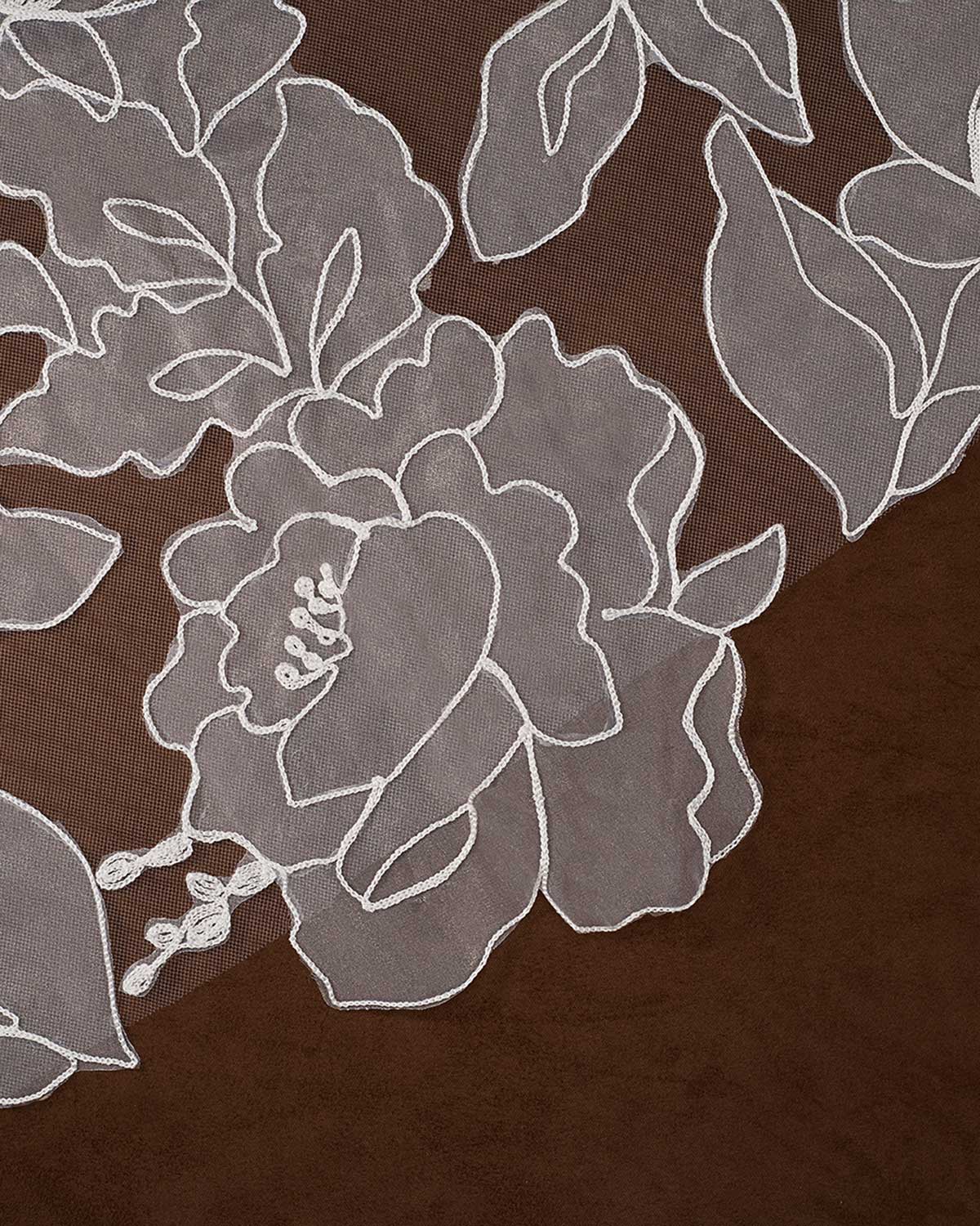 Royal Wedding Veil with Organza Flowers Cassandra Lynne A close-up of sheer floral lace fabric with white embroidered outlines over a dark brown background.
