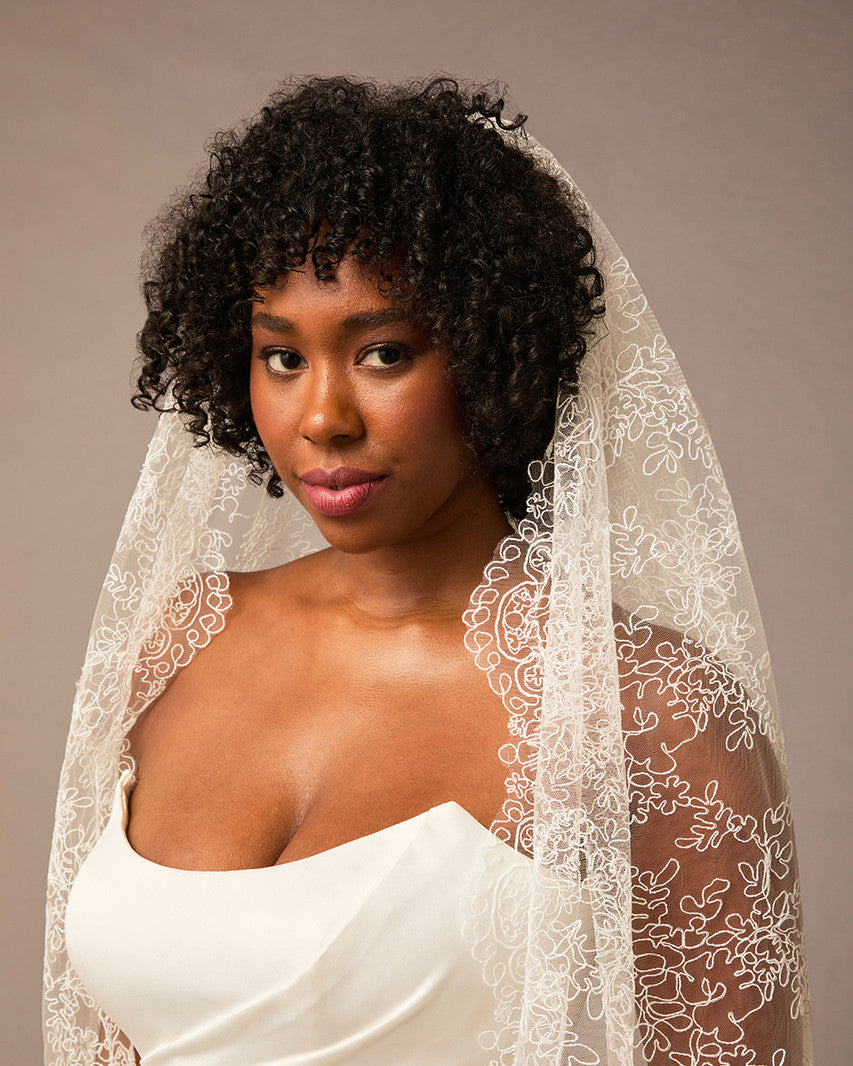 Woman wearing a white lace veil against a neutral background