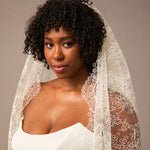 Woman wearing a white lace veil against a neutral background