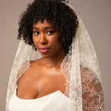 Woman wearing a white lace veil against a neutral background