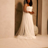 Bridal Veil with Crystal Raindrop Scatter A woman wearing a strapless ivory wedding gown with a long sheer veil stands in a softly lit architectural setting with beige walls and arches.