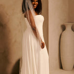Bridal Veil with Crystal Raindrop Scatter Cassandra Lynne-A woman wearing a strapless ivory wedding gown with a long sheer veil, standing in a warm beige interior with a large decorative vase in the background.