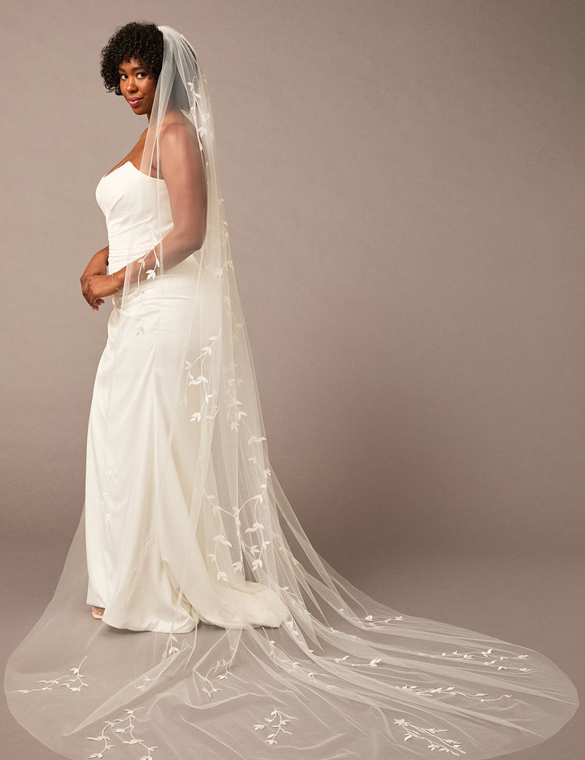 Cathedral Veil with Vine Appliques Woman wearing a wedding dress with a long veil against a brown background