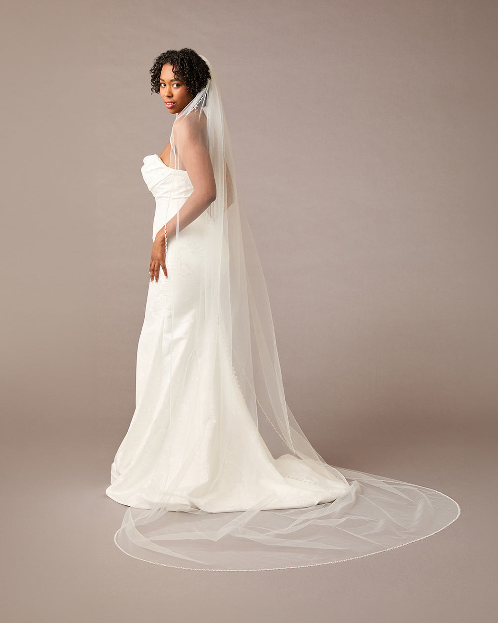 Woman wearing a  wedding dress with a long veil on a plain background Fingertip Bridal Veil with Opaque Beads and Crystals