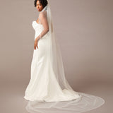 Woman wearing a  wedding dress with a long veil on a plain background Fingertip Bridal Veil with Opaque Beads and Crystals