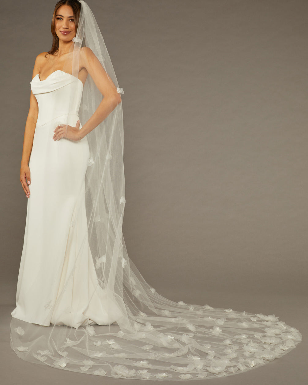 Ivory Cathedral Wedding Veil with 3D Organza Flowers Woman wearing a wedding dress with a long veil against a brown background
