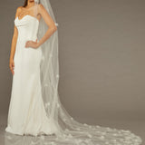 Ivory Cathedral Wedding Veil with 3D Organza Flowers Woman wearing a wedding dress with a long veil against a brown background