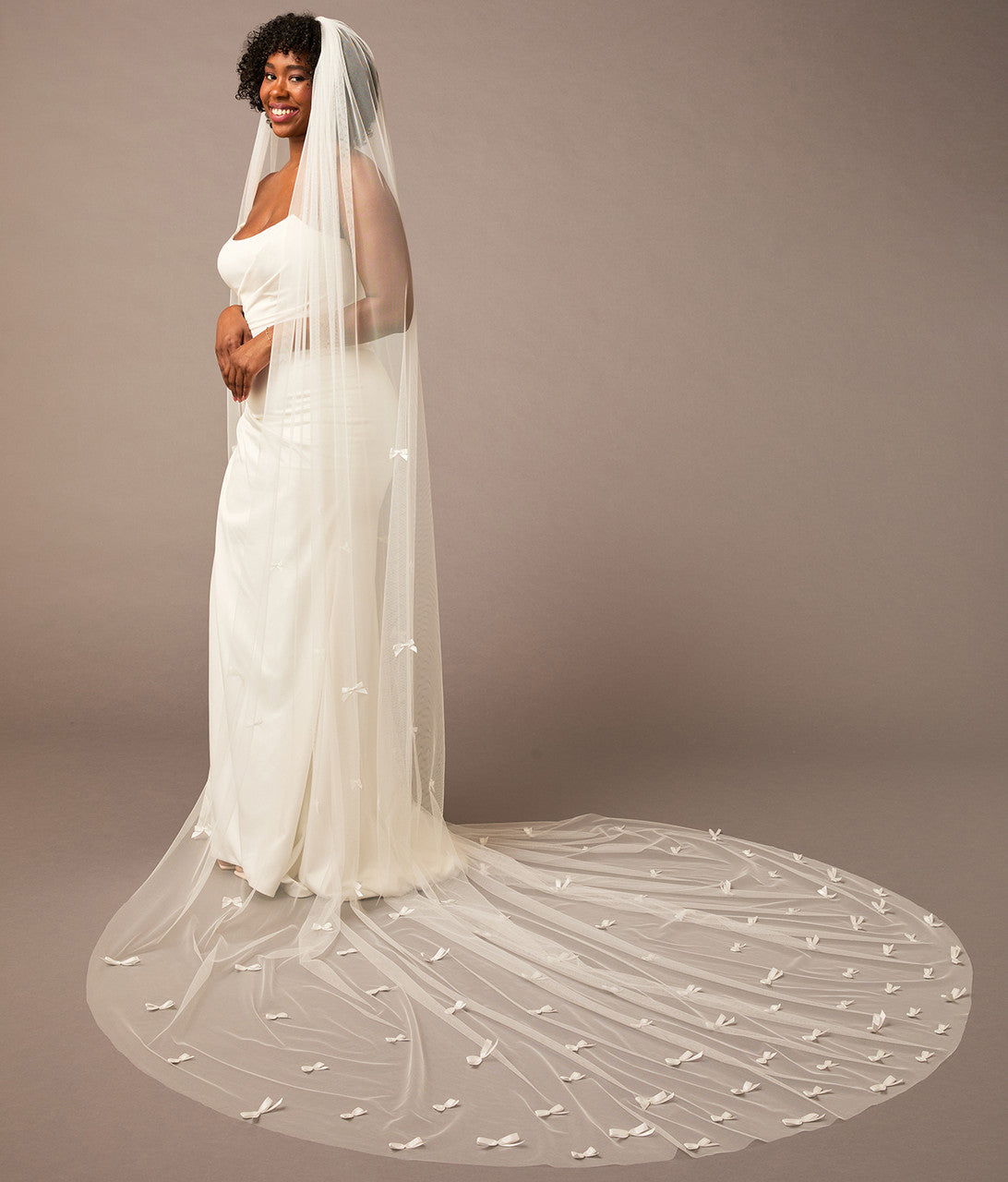Royal Cathedral Veil of Luxe Tulle and Bows Woman wearing a long wedding veil against a plain background