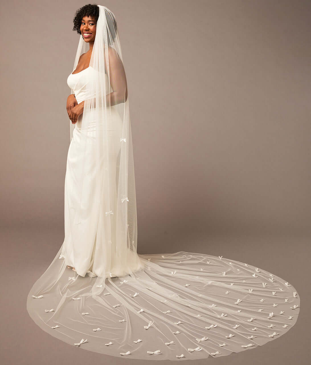 Royal Cathedral Veil of Luxe Tulle and Bows Woman wearing a long wedding veil against a plain background
