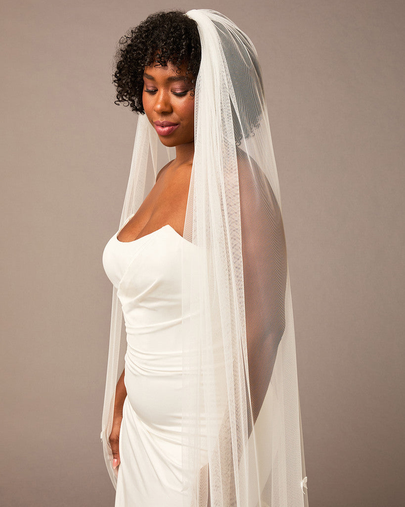Royal Cathedral Veil of Luxe Tulle and Bows Woman wearing a wedding dress with a veil against a plain background