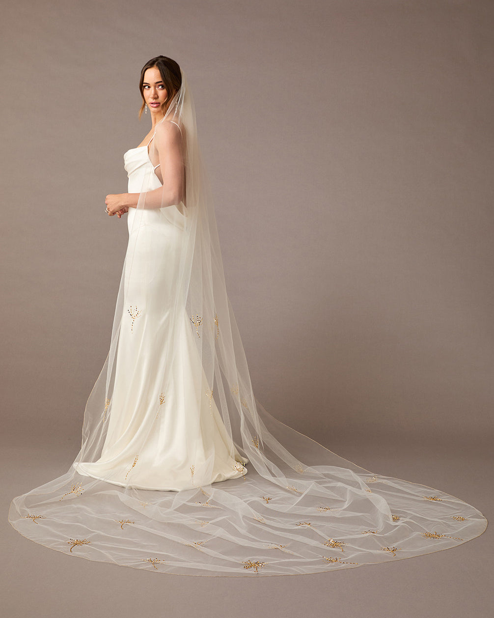 Cathedral Veil with Gold Sequined Dandelion Accents Woman wearing a wedding dress with a long veil against a brown background