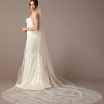 Cathedral Veil with Gold Sequined Dandelion Accents Woman wearing a wedding dress with a long veil against a brown background