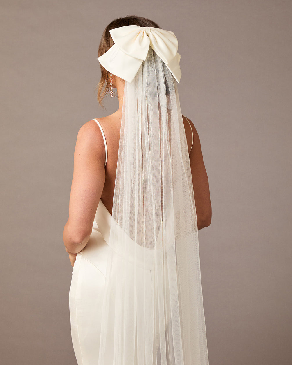 Royal Cathedral Ivory Bow Wedding Veil Woman wearing a wedding dress with a long veil and large bow on a plain background