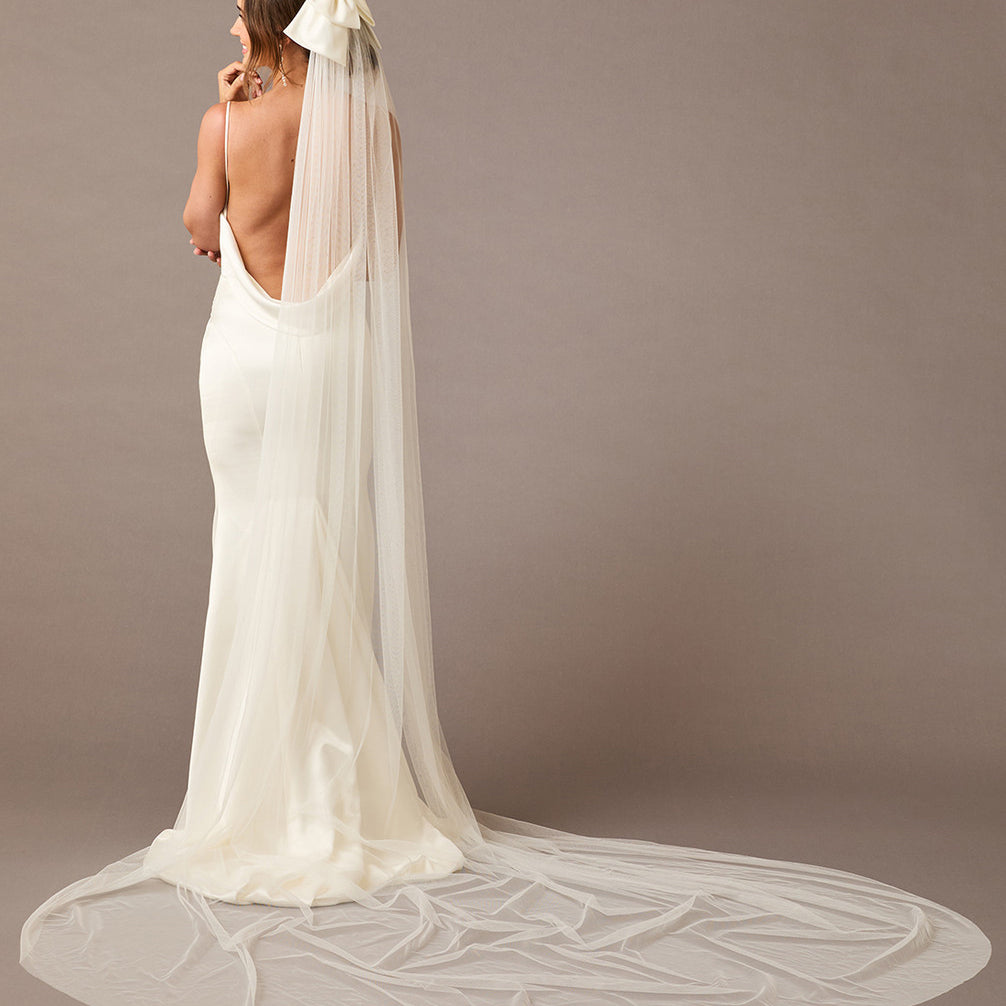 Royal Cathedral Ivory Bow Wedding Veil Woman wearing a long  wedding veil with a bow on a brown background