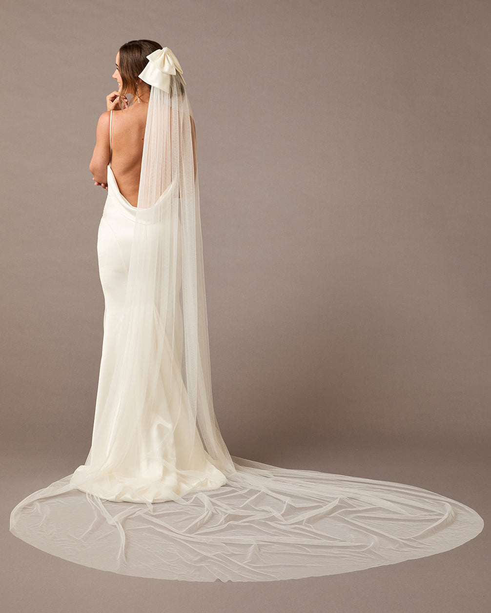 Royal Cathedral Ivory Bow Wedding Veil Woman wearing a long  wedding veil with a bow on a brown background