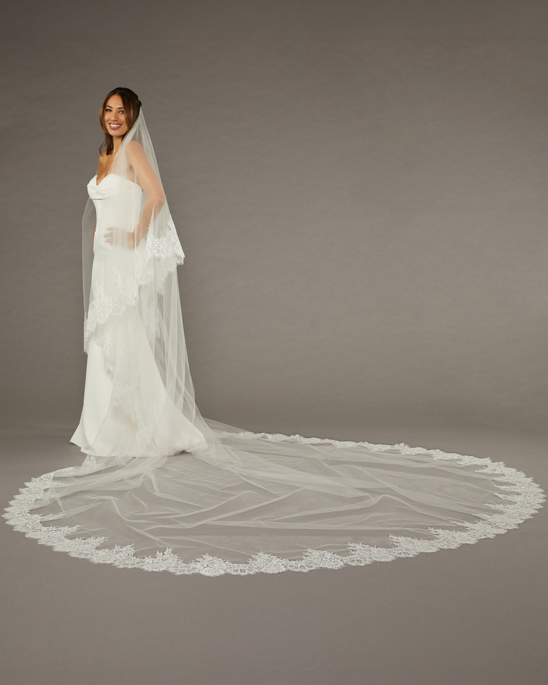 Two Layer Chantilly Lace Cathedral Bridal Veil Woman wearing a wedding dress with a long veil on a gray background